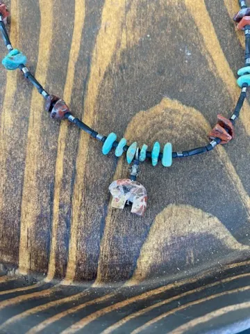 Close detail of a beaded necklace with a small carved stone bear pendant, turquoise chips and red jasper on black beads