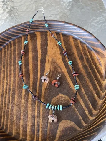 Matched set laid out in a wooden bowl: a long necklace of turquoise, jasper and black beads with a carved stone bear pendant, and two matching earrings