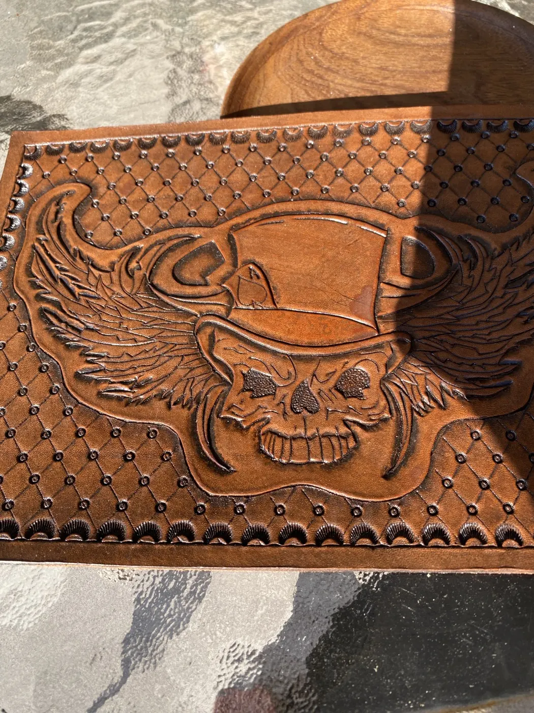 Large hand-tooled leather panel of a winged skull wearing a top hat, surrounded by a stamped diamond lattice border, in rich saddle brown