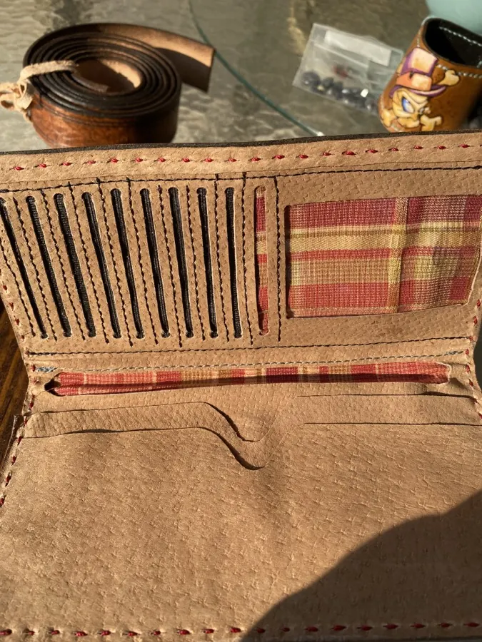 Open interior of a handmade leather wallet showing laced card slots, a red plaid fabric-lined pocket, and red stitching along every edge